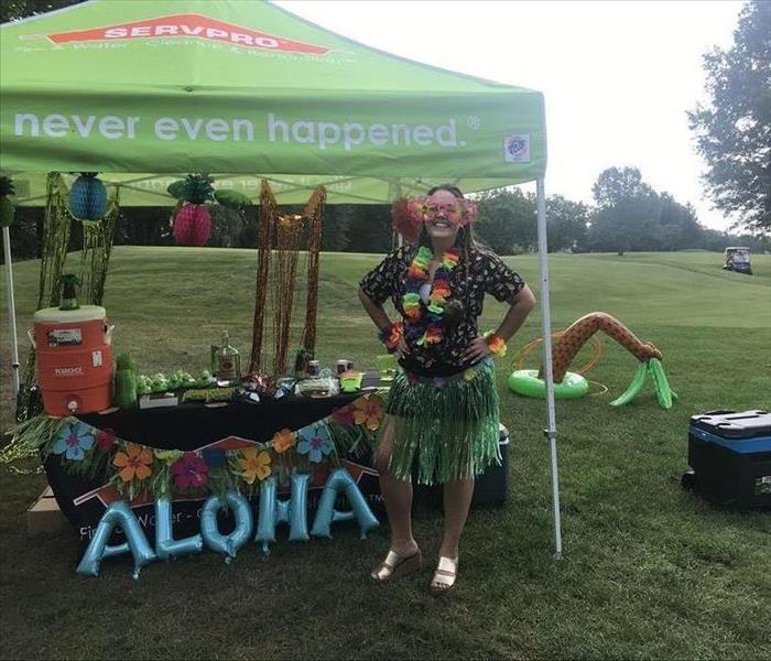 female employee in hula skirt under green tent on golf course