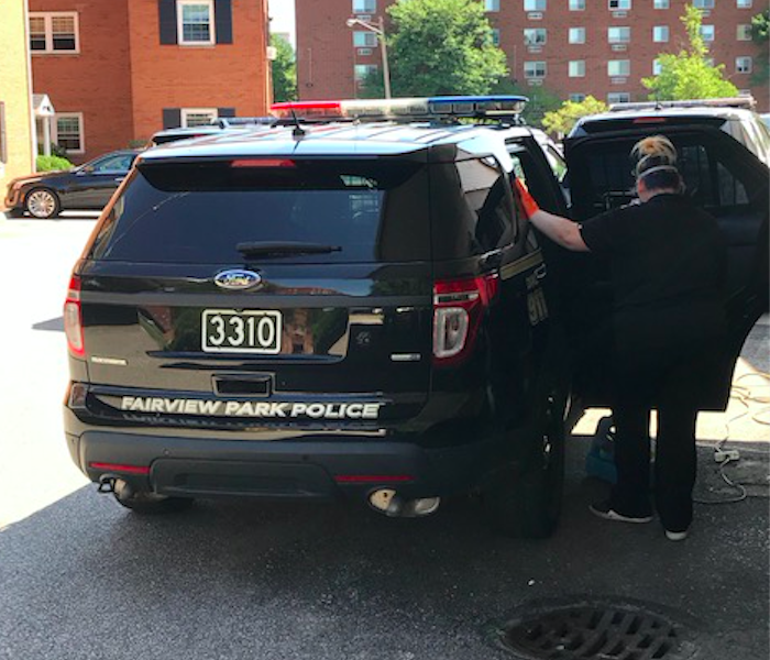 female employee in PPE cleaning police car